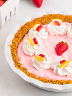 A deliciously pink no bake Kool-Aid pie with garnishes of whipped cream, lemon wedges and strawberries