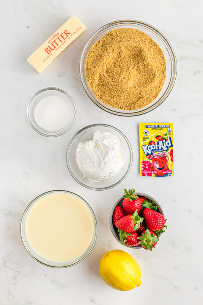 Sweetened condensed milk, strawberries, a full lemon, a Kool-Aid packet and cool whip in bowls against white background