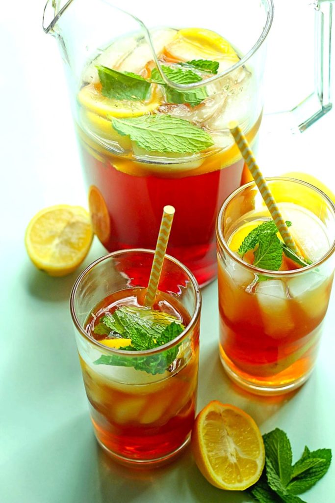 A pitcher filled with Southern sweet tea along with two glasses of tea with ice, lemon slices and mint