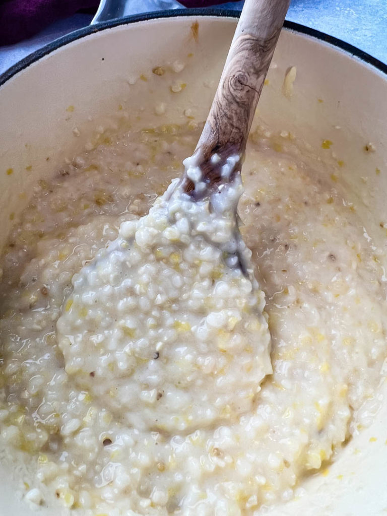 a pot of cooked grits with a wooden spoon