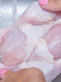 Woman washing raw frozen hen in kitchen sink. Cooking chicken at home. Close-up, selective focus.
