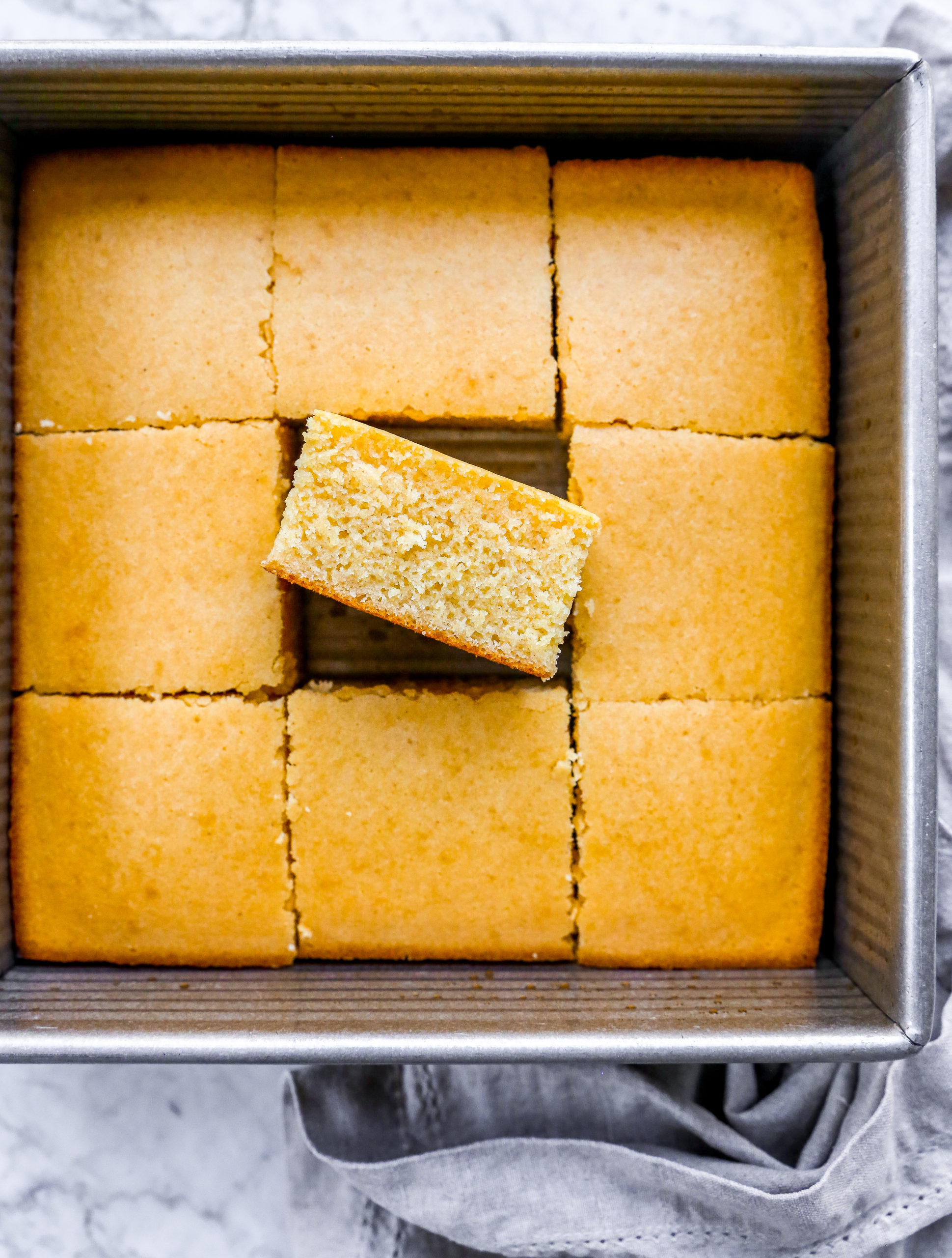 A pan of sliced cornbread with a fluffy slice on its side.