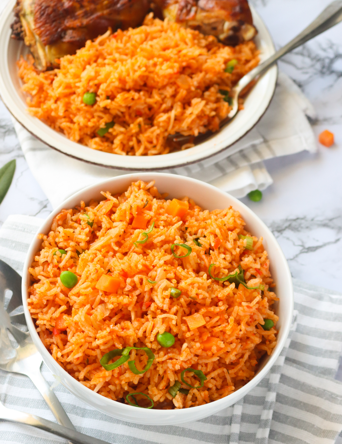 Two bowls of Jollof Rice with chicken in the background