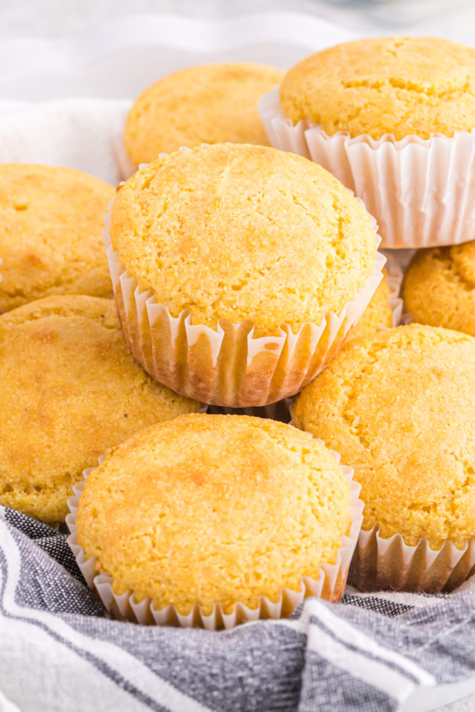 A stack of corn muffins inside of a napkin lined basket ready to enjoy.