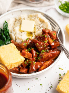 bowl of bbq tofu, cornbread, mashed potato and collard greens with a fork