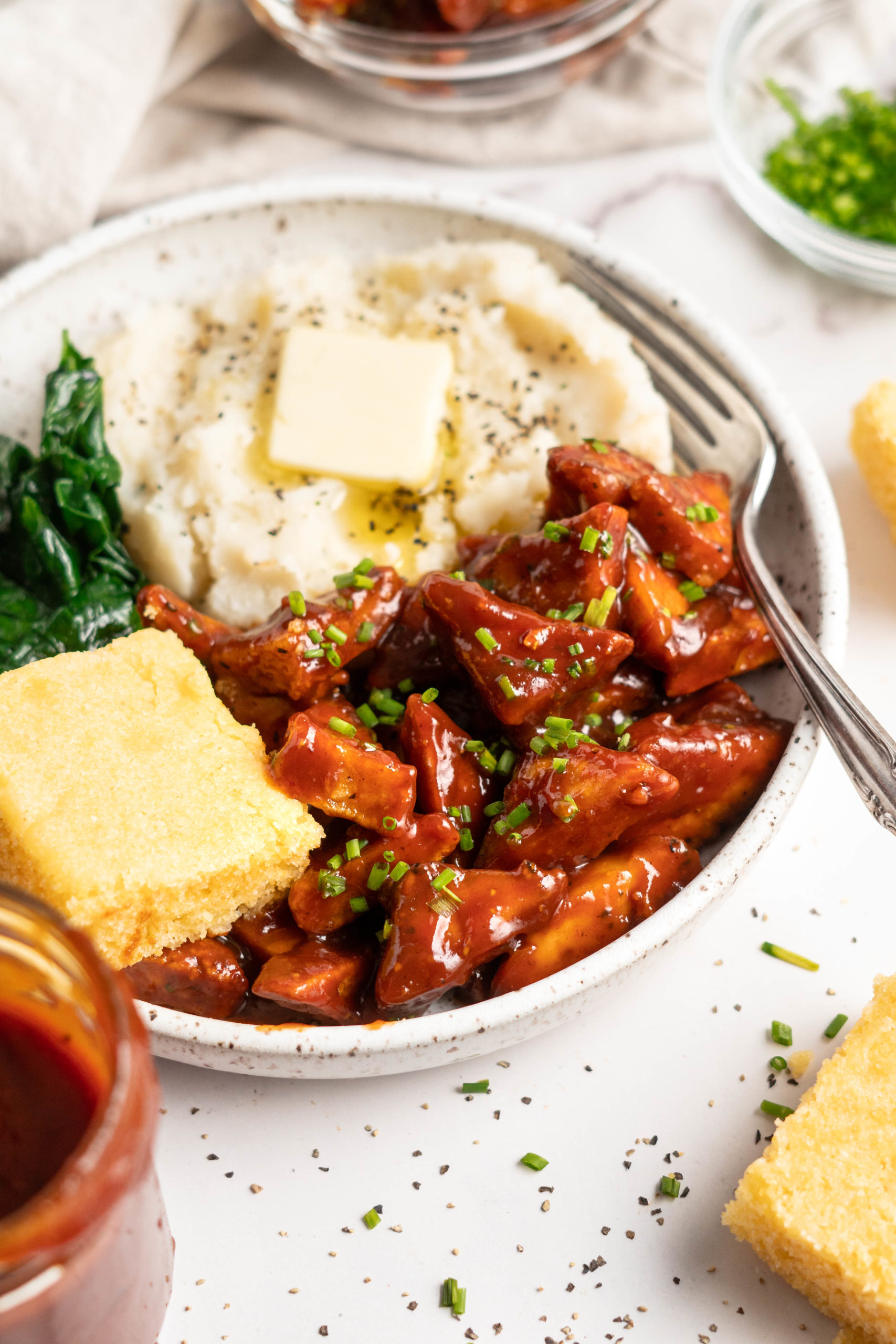 bowl of bbq tofu, cornbread, mashed potato and collard greens with a fork