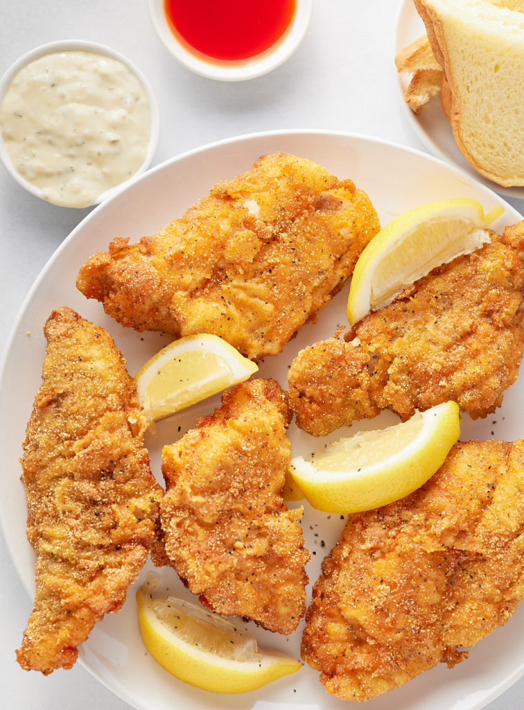 fried catfish filets on white plate with lemon wedges