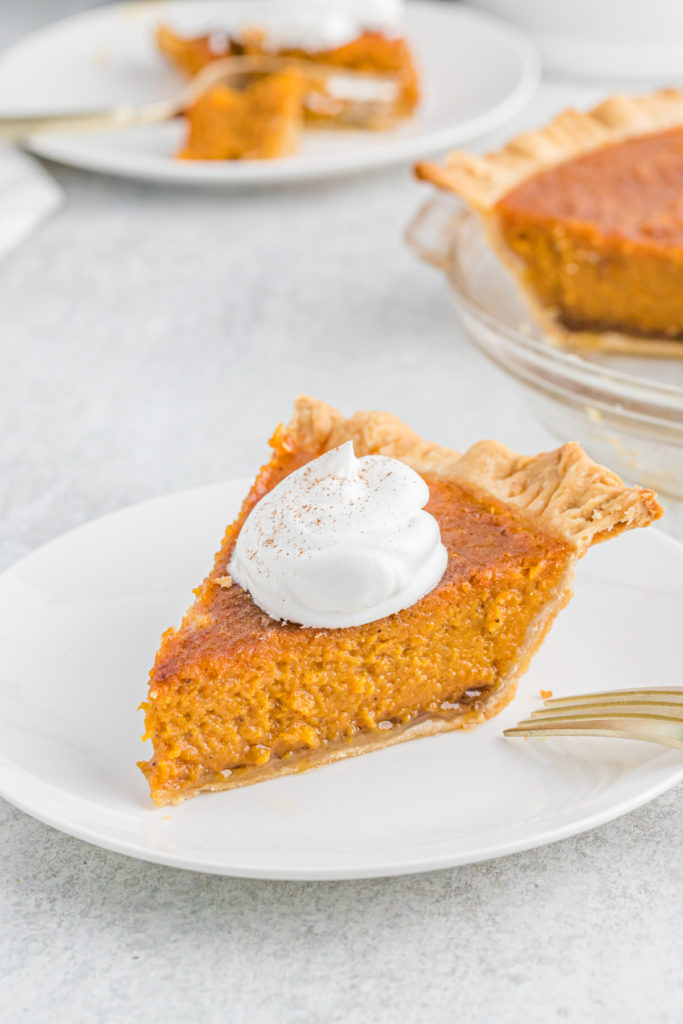A slice of Patti Labelle sweet potato pie on a white plate with whipped cream ready to serve.