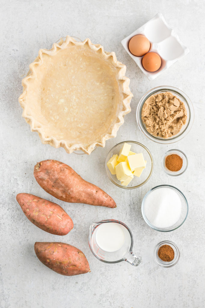 An overhead of sweet potatoes, butter, sugars and spices with an unbaked pie crust before making a pie.