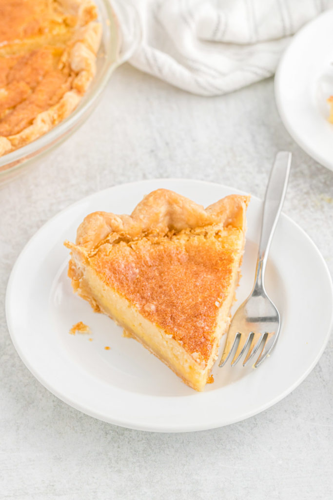 A slice of Southern buttermilk pie on a white plate with a fork ready to serve.