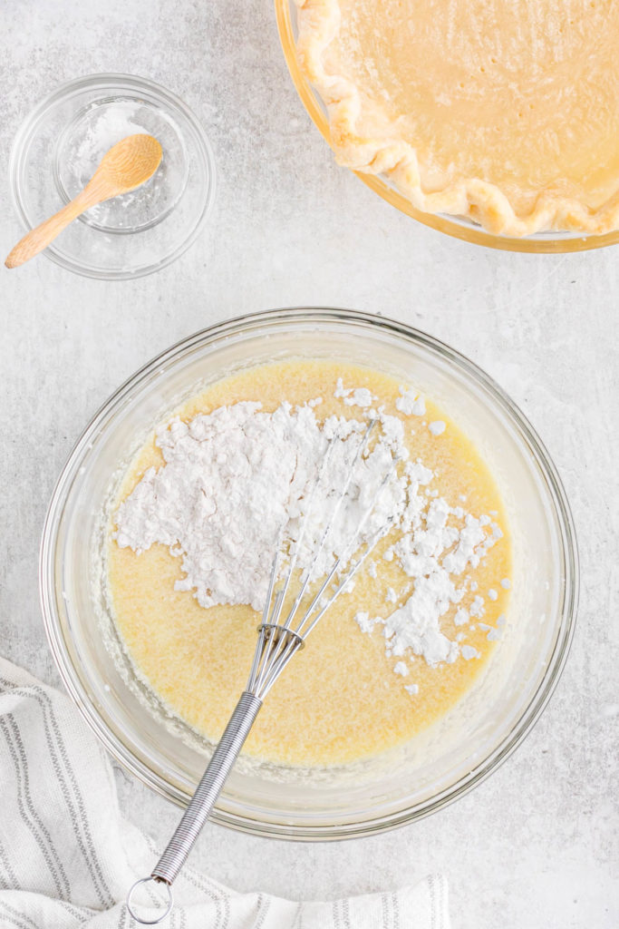 Pie mixture being whisked together with flour and cornstarch in a clear bowl.