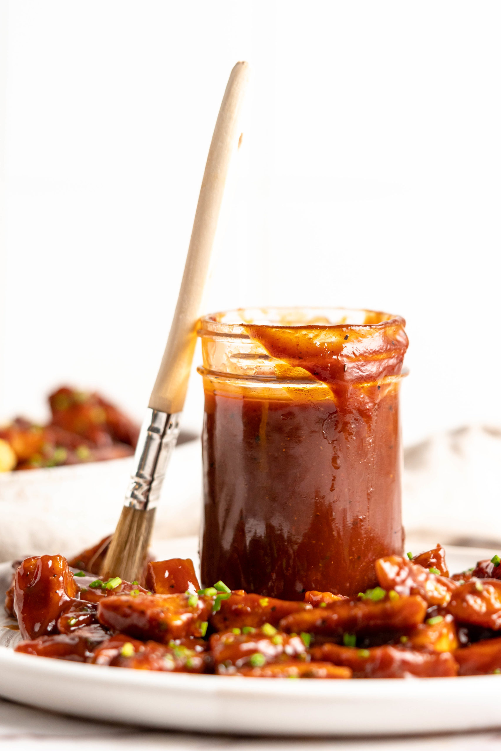 Barbecue sauce in jar, set on plate of BBQ tofu with brush