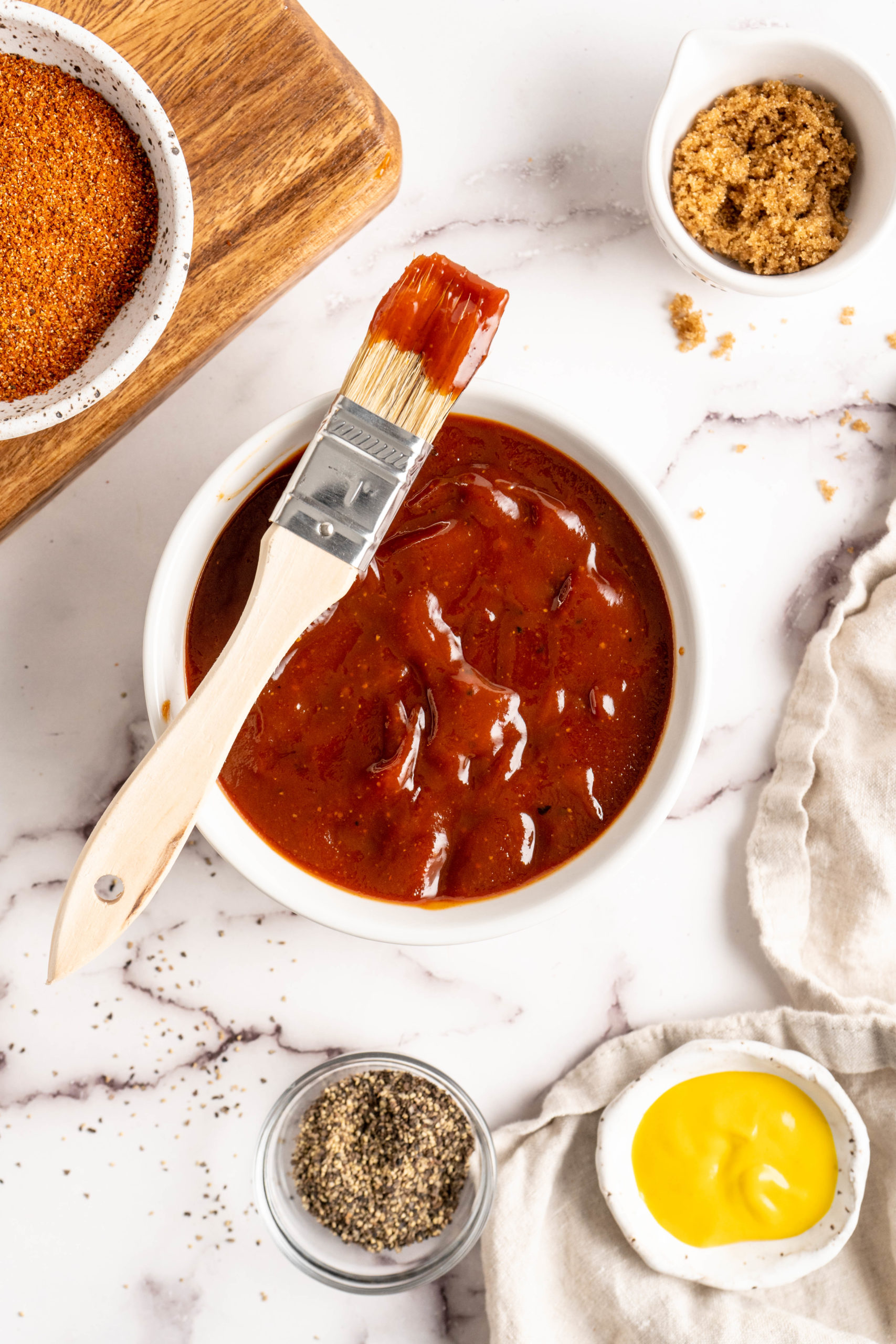 Bowl of barbecue sauce with brush, surrounded by sauce ingredients