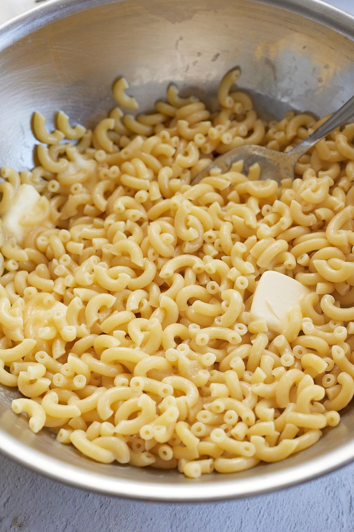 boiled macaroni noodles with butter being tossed in