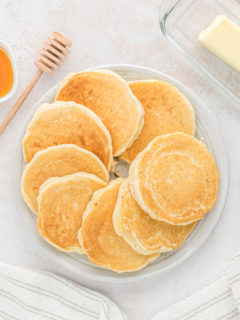 Scattered hoe cakes on a white plate with honey and butter nearby
