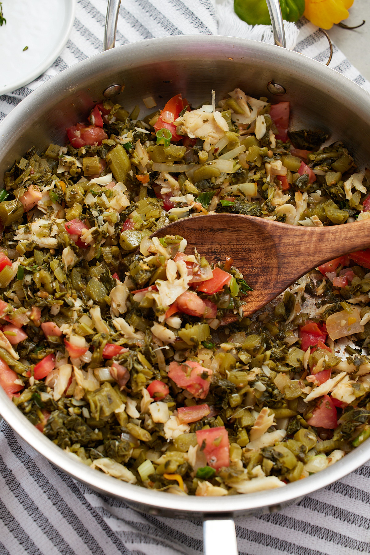 callaloo and saltfish in skillet with wooden spoon sticking out and scotch bonnet peppers on the side