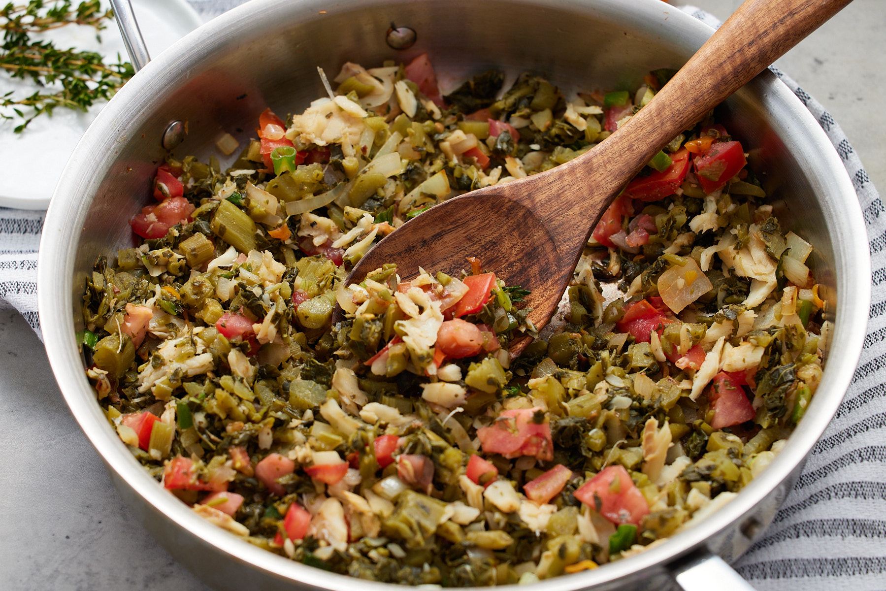 callaloo and saltfish recipe in a skillet with a wooden spoon sticking out and thyme on the side