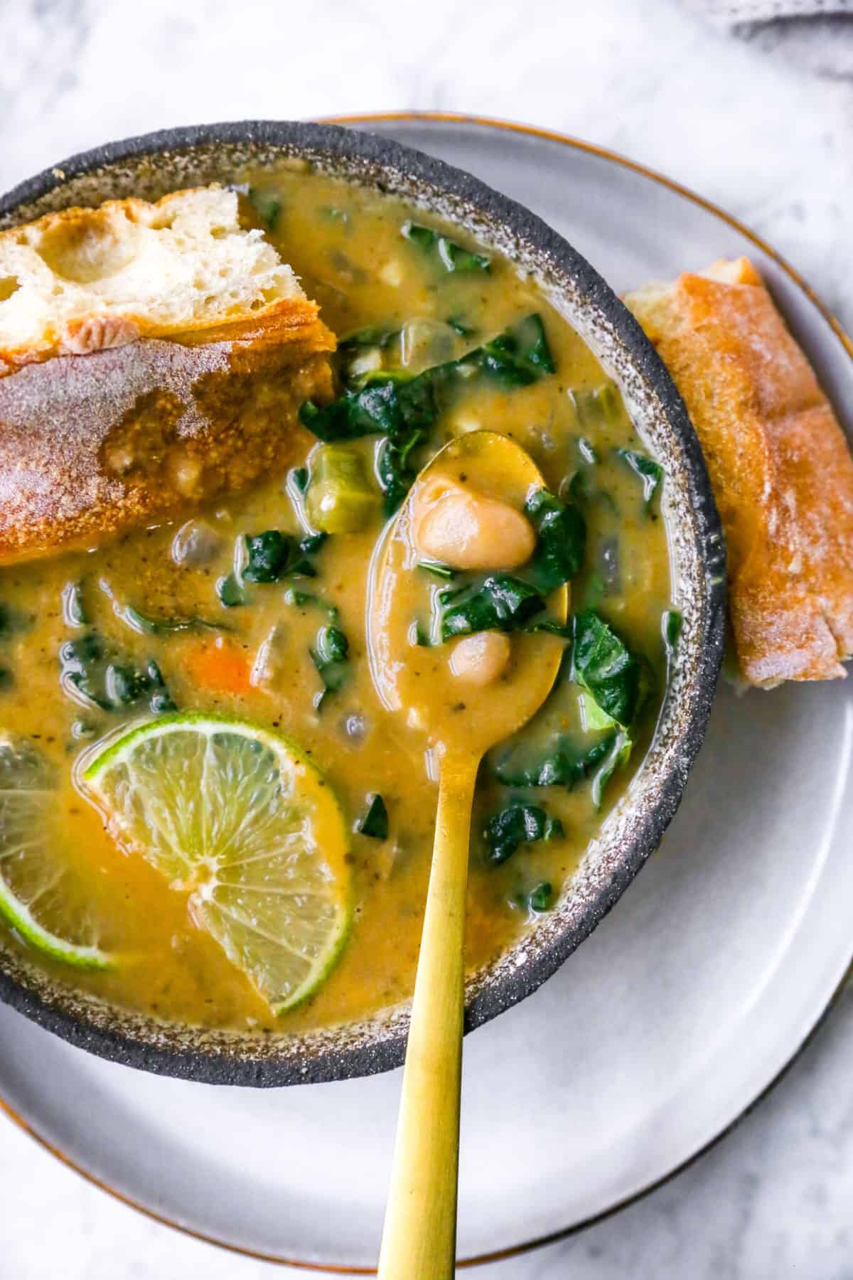 Bowl of white bean soup on plate with sliced lime and pieces of bread