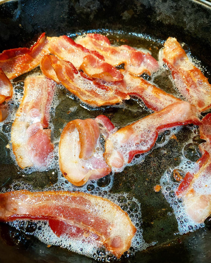bacon cooking in a cast-iron skillet