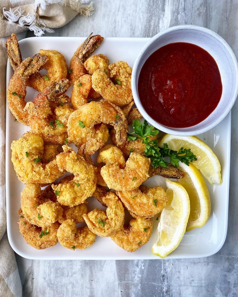 fried shrimp on a white plate with lemon wedges & cocktail sauce in a bowl