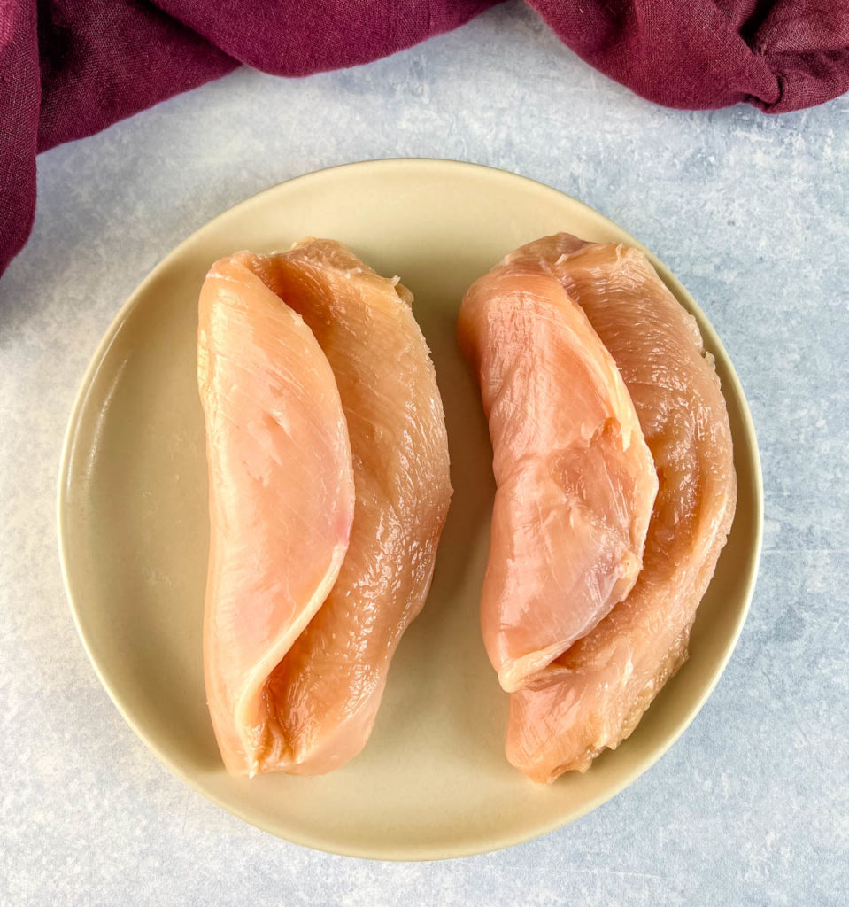 raw skinless chicken breasts sliced in half on a plate