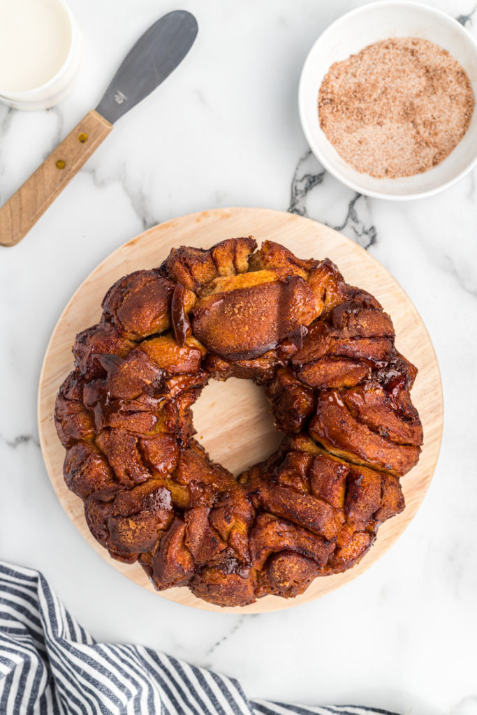A cinnamon roll cake inverted from a bundt pan with cinnamon sugar in a white bowl