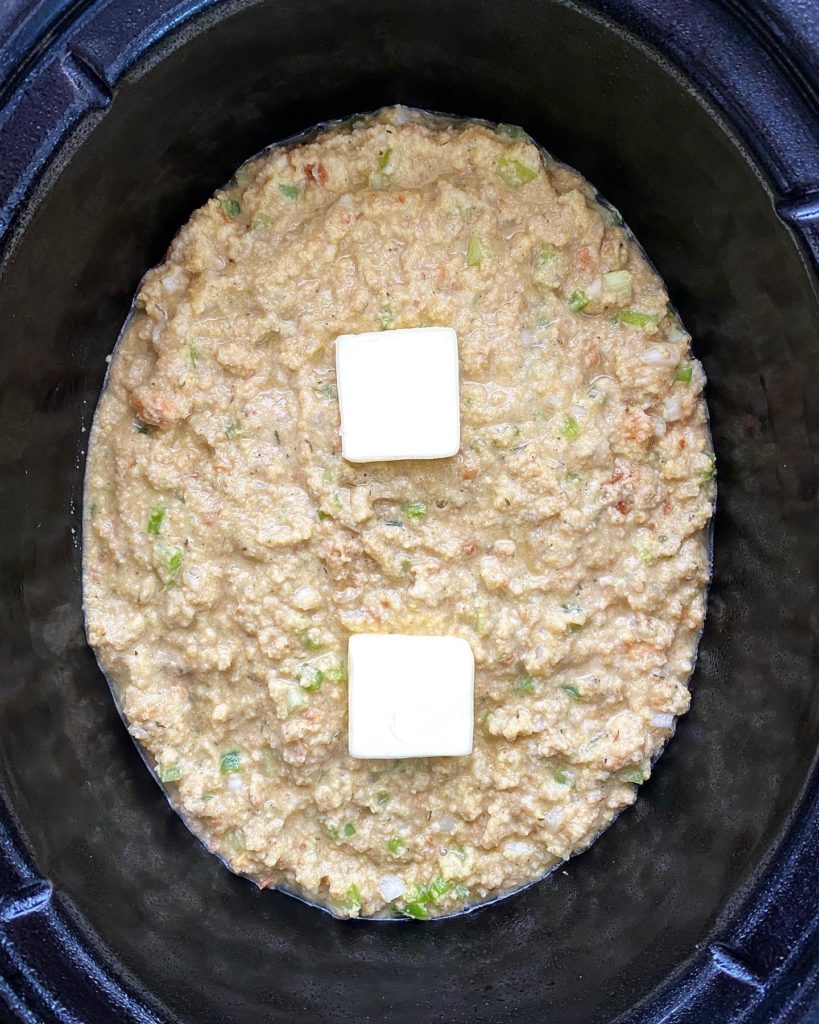 uncooked cornbread dressing in the crockpot with tablespoons of butter on top