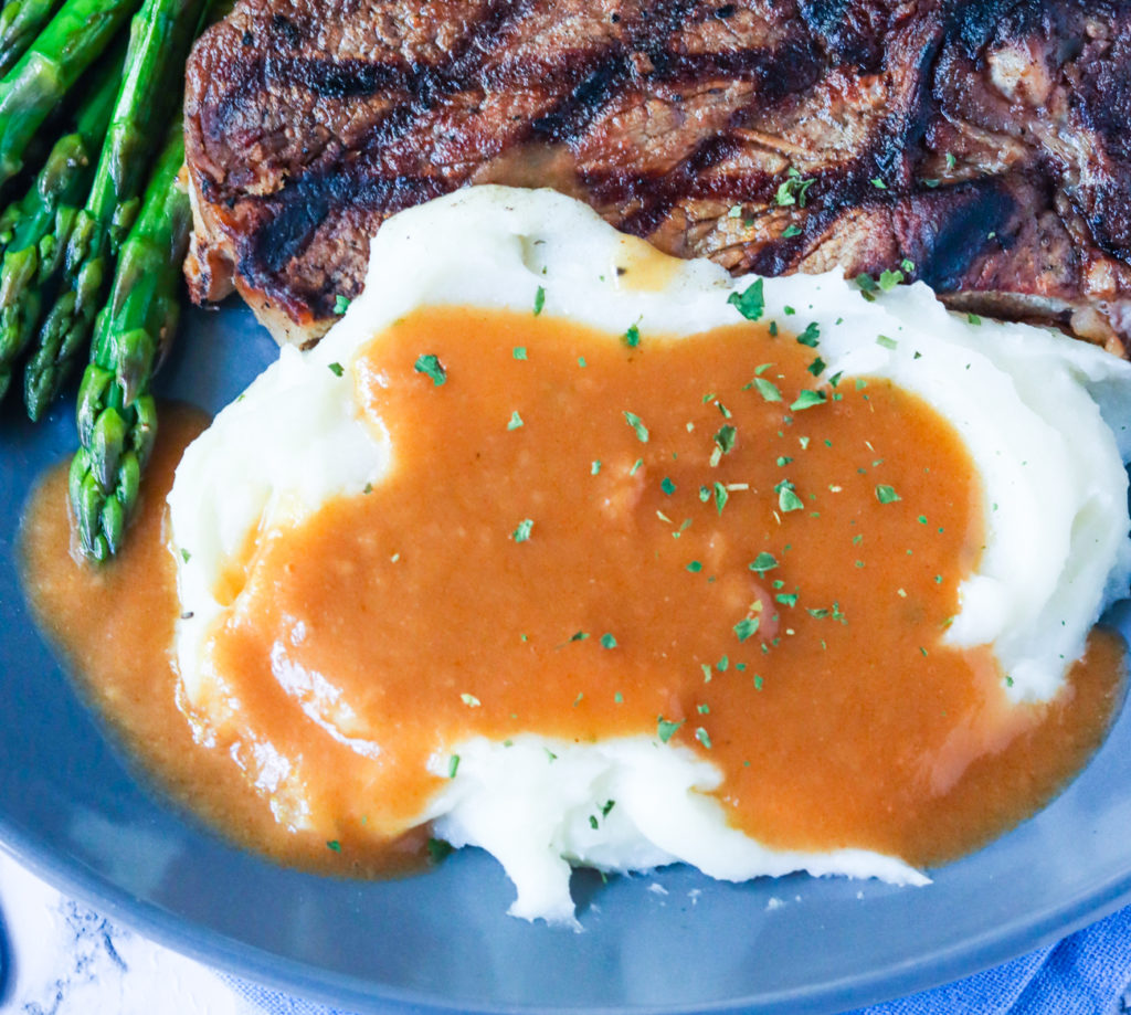 Brown gravy over mashed potatoes with asparagus and steak