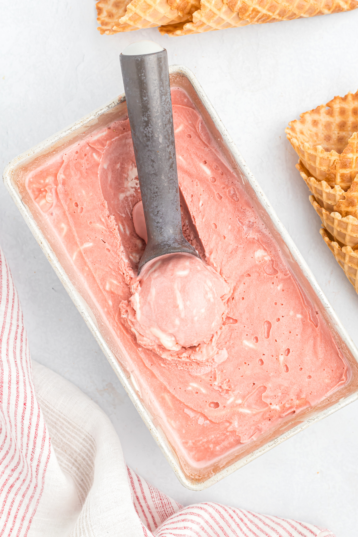 A red colored ice cream being scooped to serve in a waffle cone