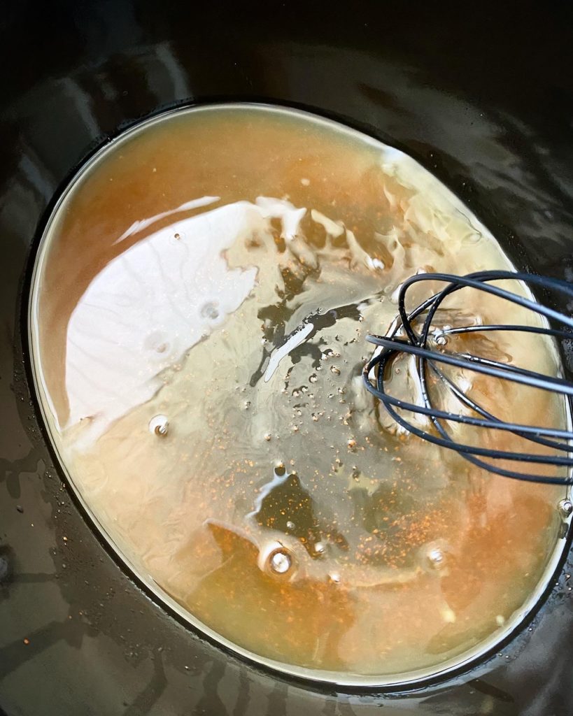 pineapple juice and brown sugar being mixed in the base of the slow cooker with a black whisk