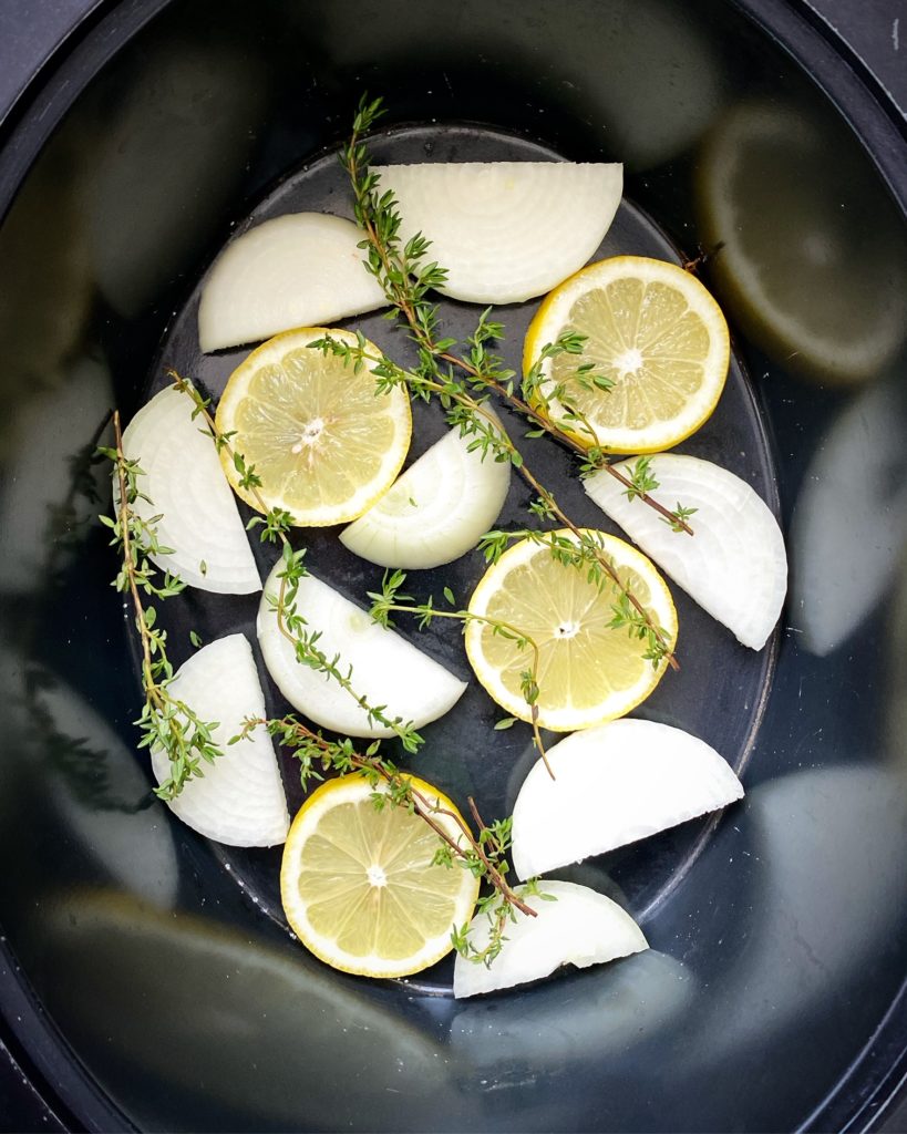 sliced lemon, onion, and fresh herb in the bottom of the slow cooker