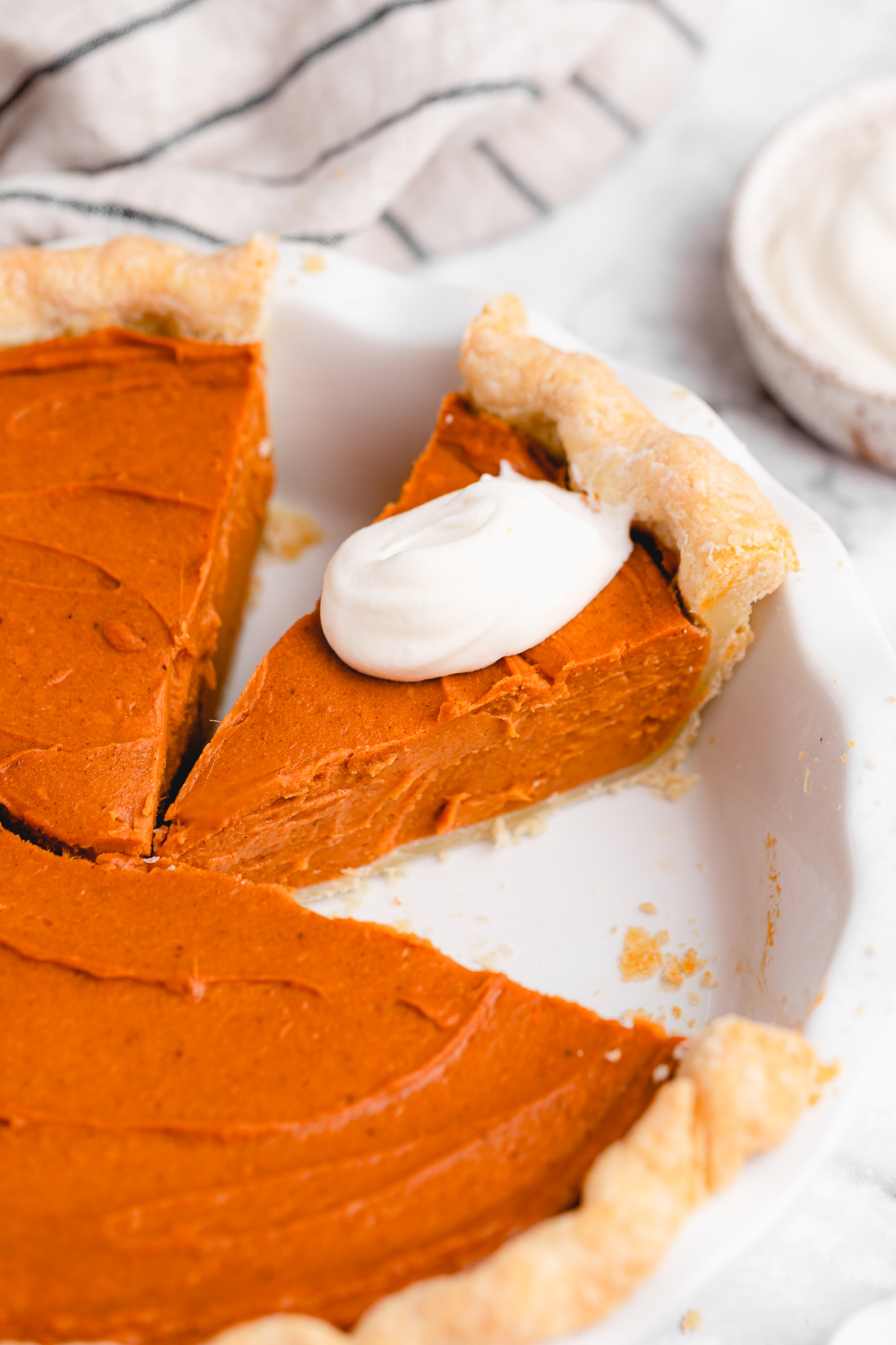 Whole vegan sweet potato pie with slice topped with coconut cream