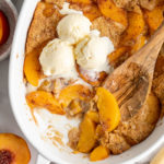 Overhead view of peach cobbler in dish with scoops of ice cream