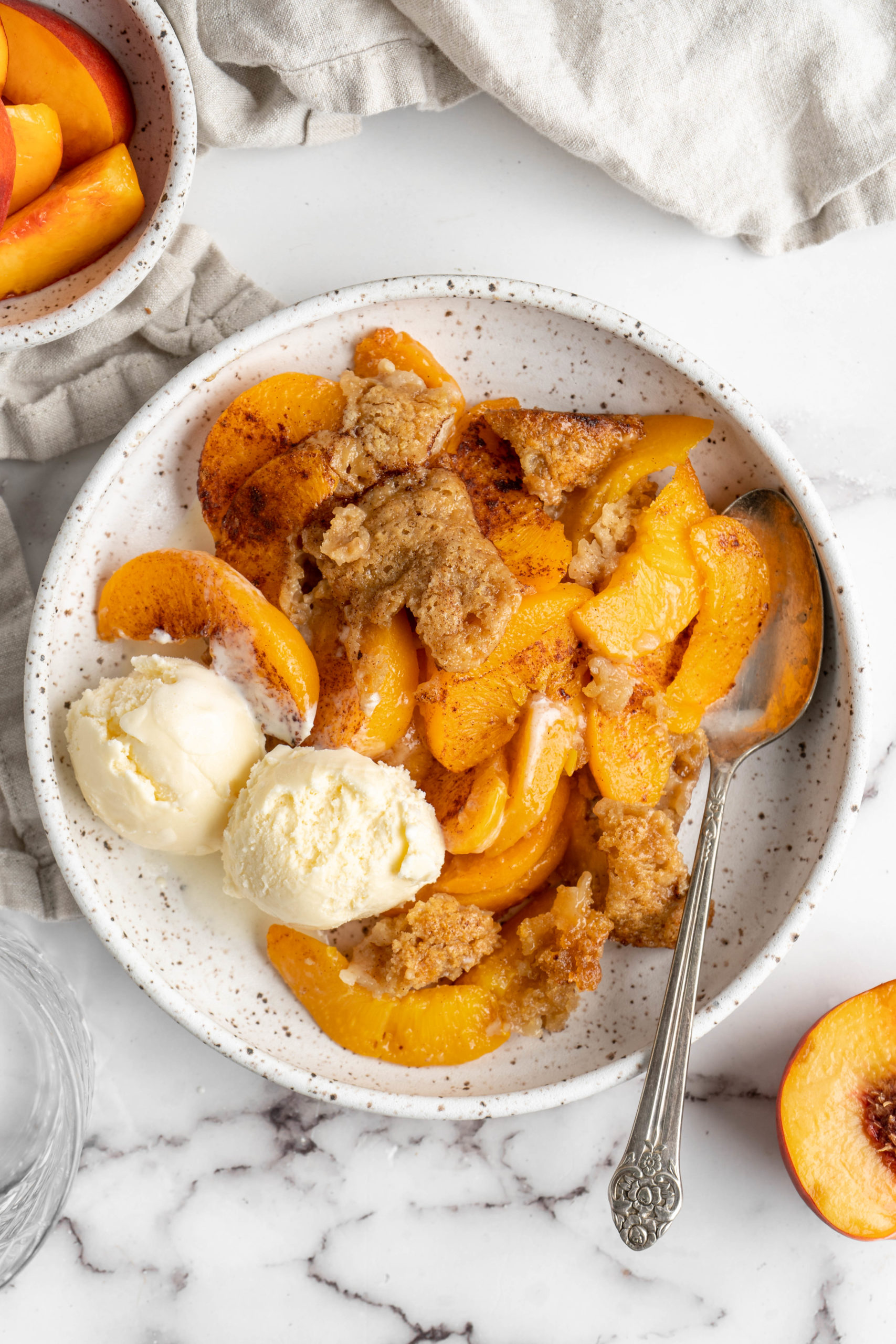 Overhead view of peach cobbler in bowl with scoops of ice cream