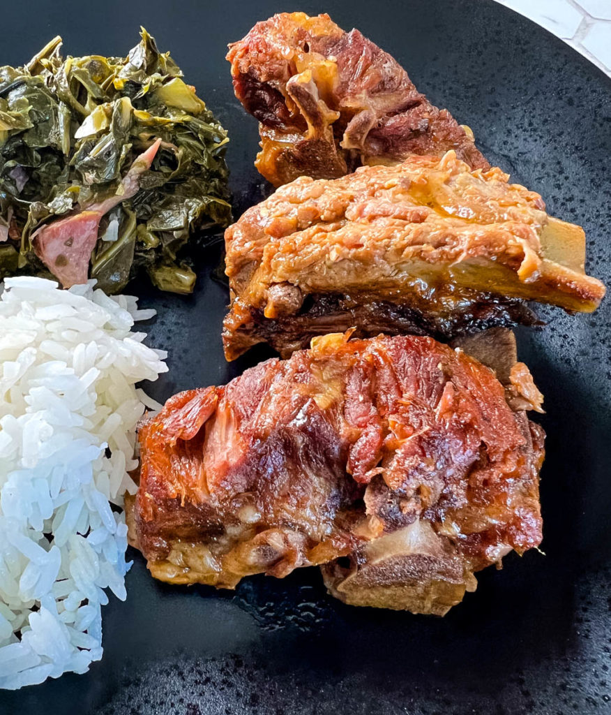 pork neck bones on a black plate with rice, collard greens, and cornbread