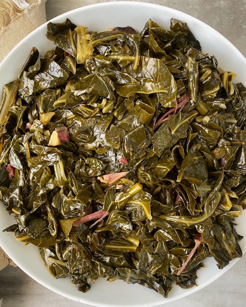 cooked collard greens with pieces of ham hocks in a white bowl