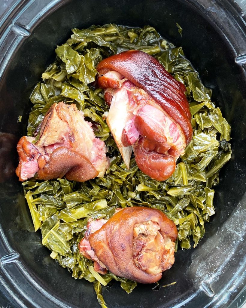 cooked collard greens in the slow cooker with ham hocks on top