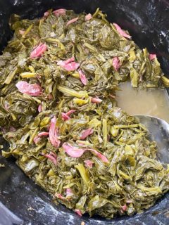 cooked greens with shredded ham hock meat in the slow cooker with a spoon