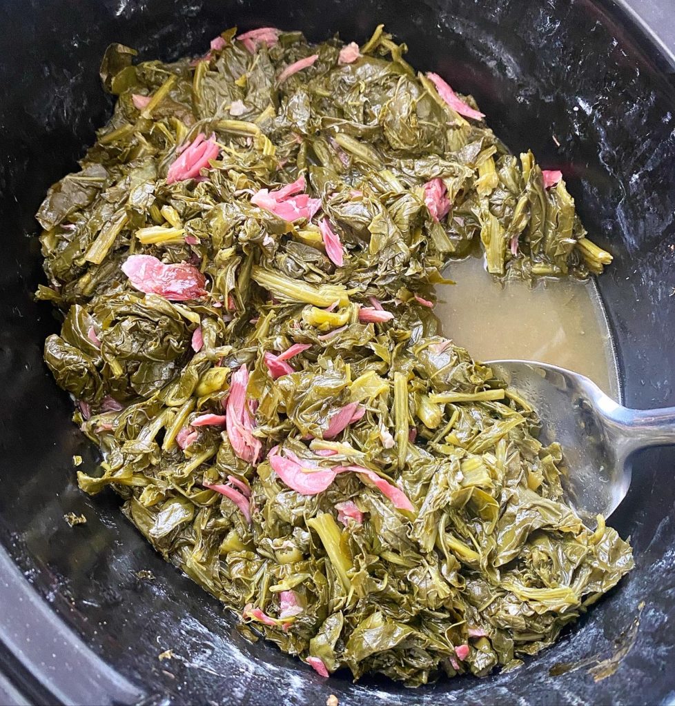 cooked greens with shredded ham hock meat in the slow cooker with a spoon