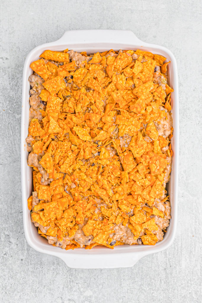 Crumbled doritos placed on top of a casserole before baking