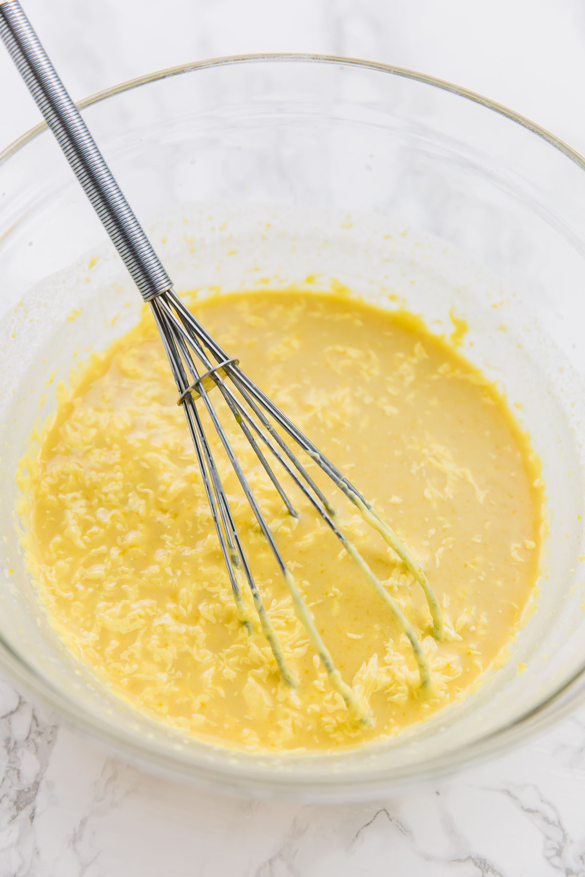 A bowl of the wet ingredients for vegan cornbread muffins, including pumpkin puree, with a whisk in it
