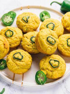 A plate full of vegan cornbread muffins, with jalapeño slices on top, and raw jalapeño slices on the plate