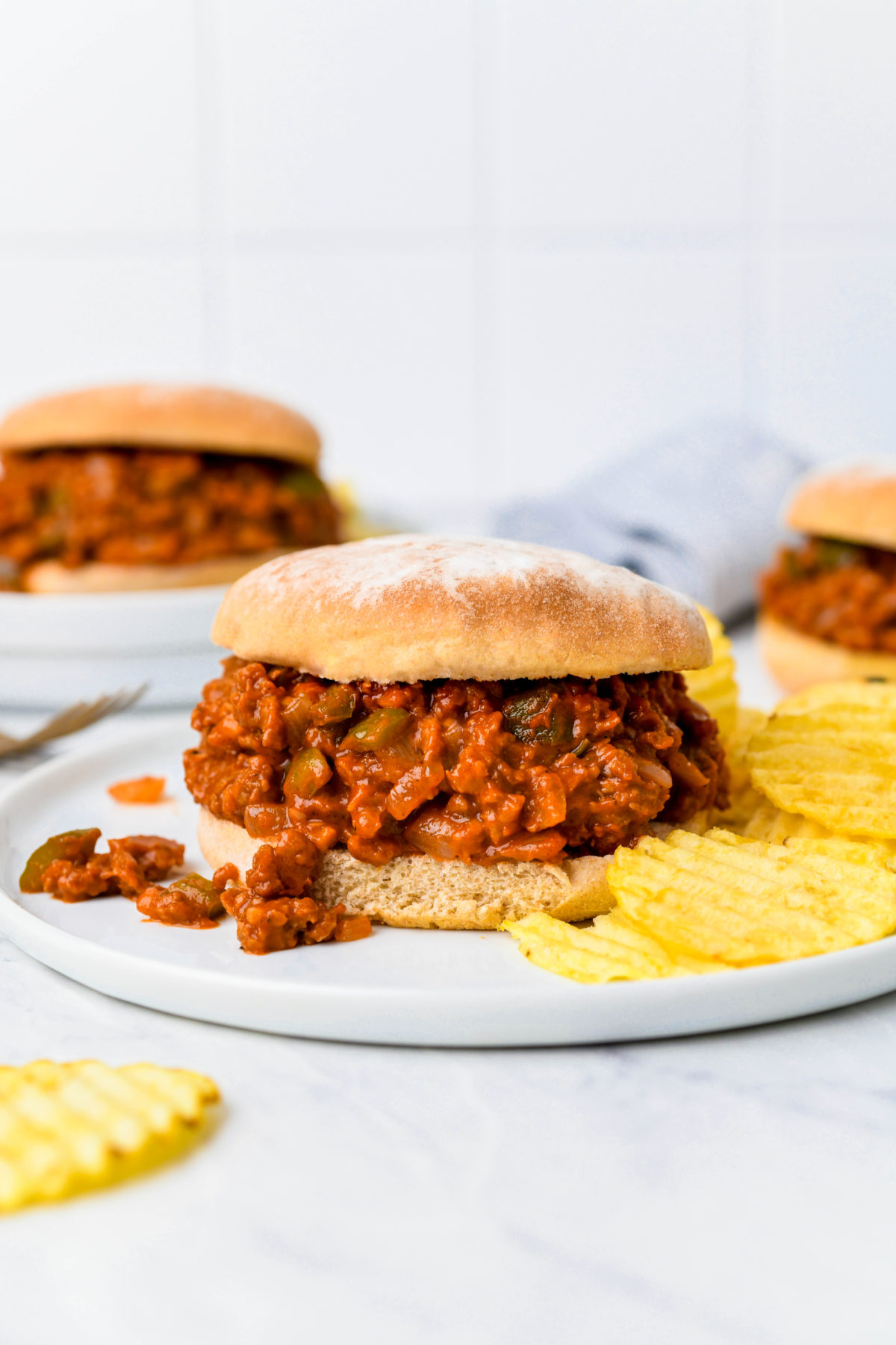 A vegan sloppy joe sandwich on a plate with potato chips and sloppy joe filling spilling out