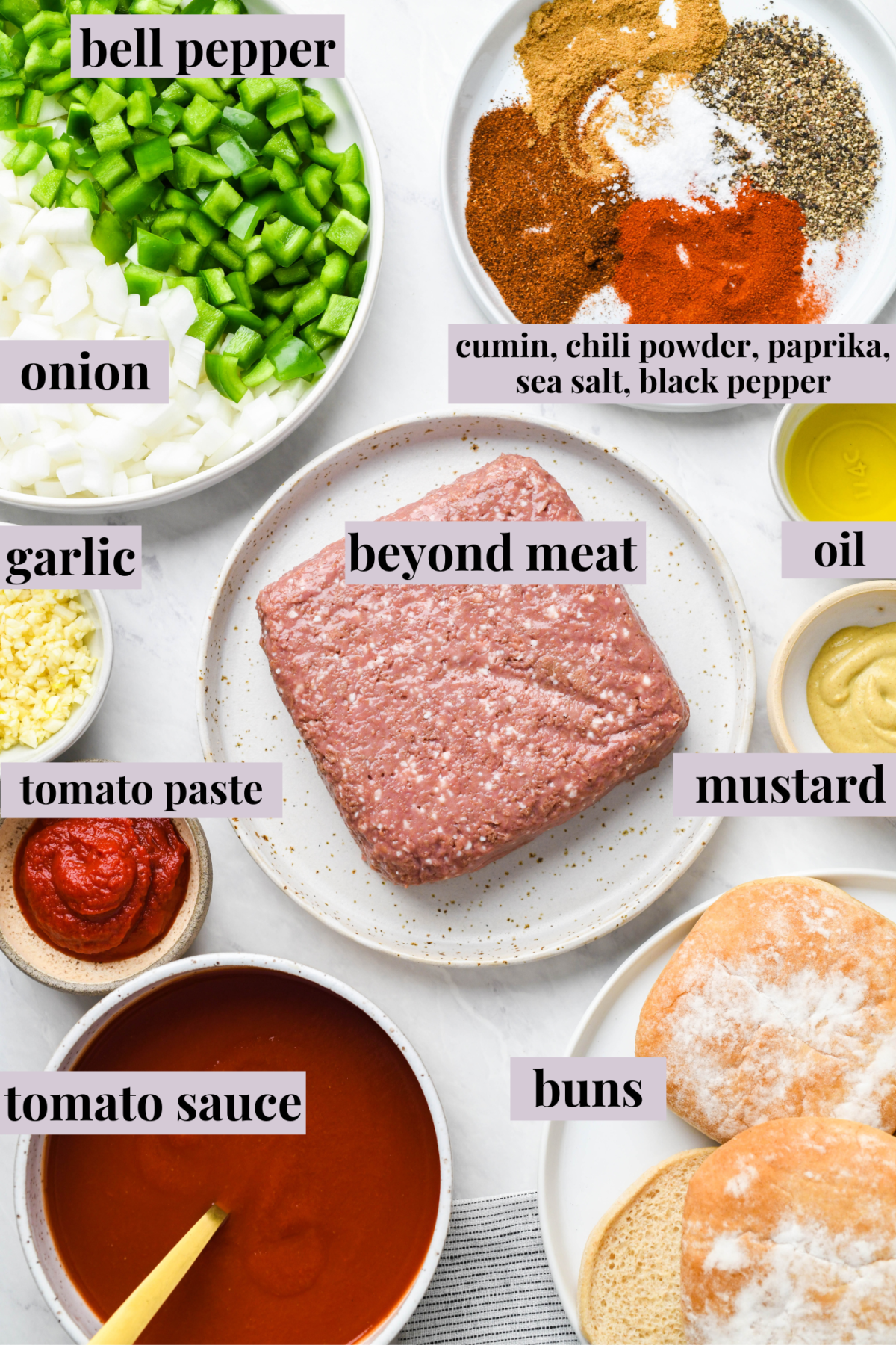 Overhead view of labeled, uncooked ingredients for vegan sloppy joes: Beyond meat, onions, bell peppers, garlic, cumin, chili powder, paprika, sea salt, black pepper, mustard, tomato paste, tomato sauce, oil, and buns