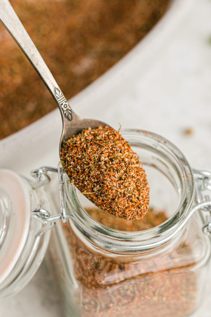 A spoon of cajun spice being lifted from a glass jar