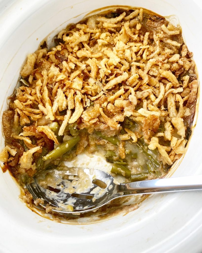 overhead shot of green bean casserole in a white slow cooker with a spoon in it & a scoop missing