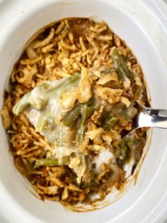 overhead shot of uncooked green bean casserole in a white slow cooker with a spoon