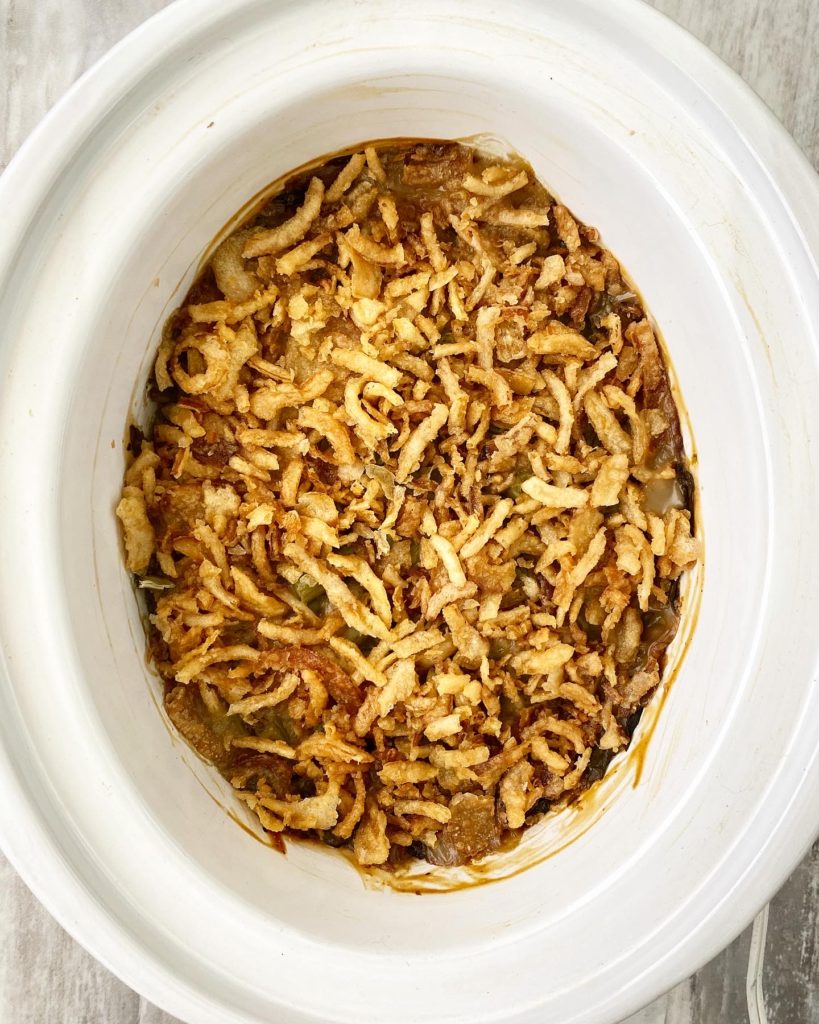 overhead shot of cooked green bean casserole in a white slow cooker with french fried onions on top