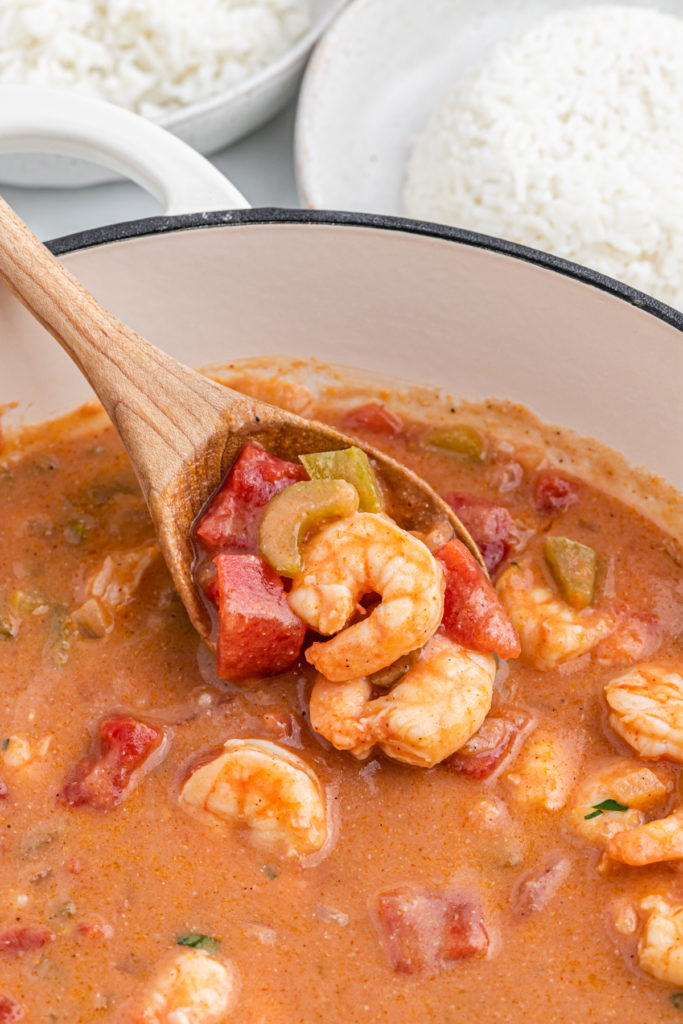 A wooden spoon filled with shrimp etouffee ready to serve.