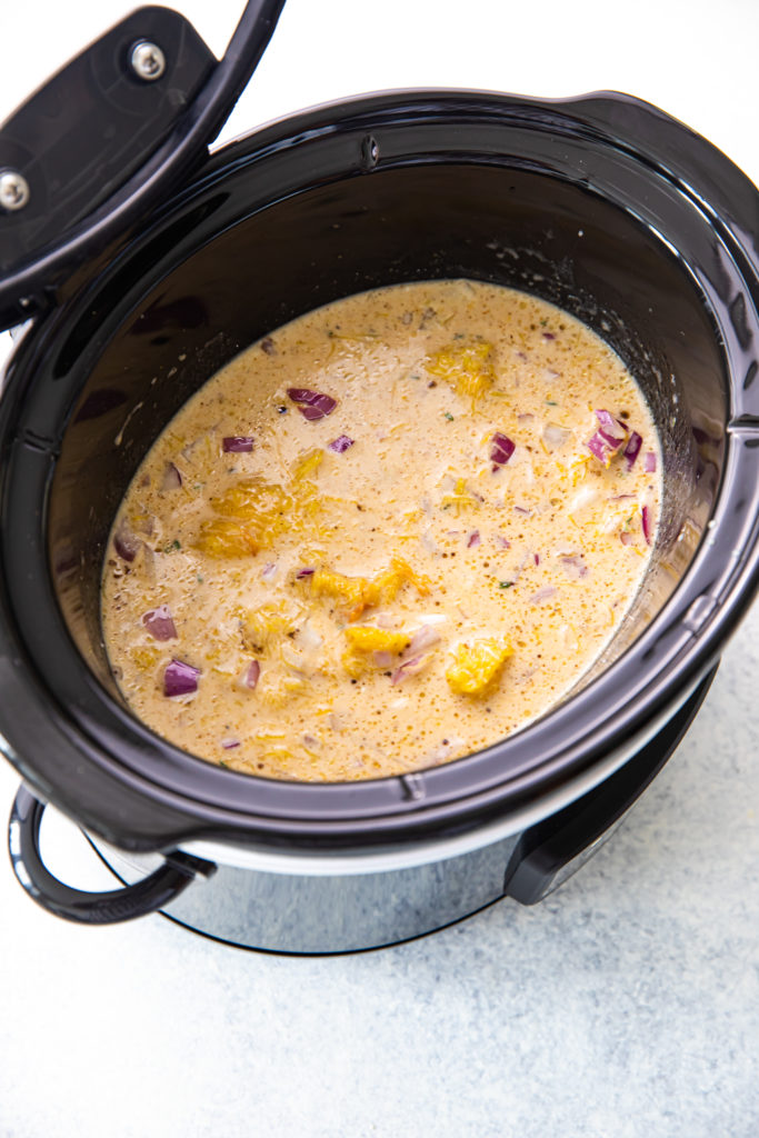 A slow cooker filled with cooked pumpkin soup that hasn't been blended